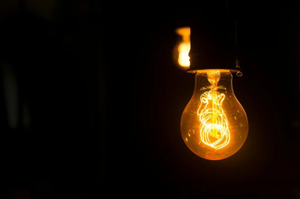 pexels-photo-1556704-1556704 Close-up view of an illuminated vintage light bulb with glowing filament against a dark background.