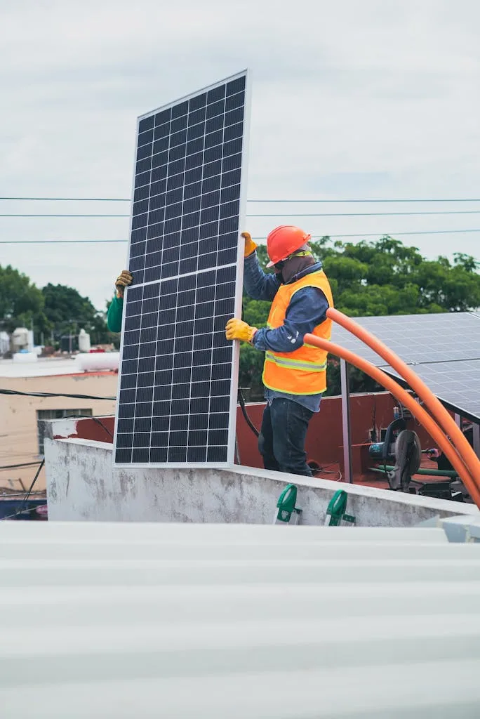 Photo by Los Muertos Crew A technician in safety gear installs a solar panel on a rooftop, promoting renewable energy.