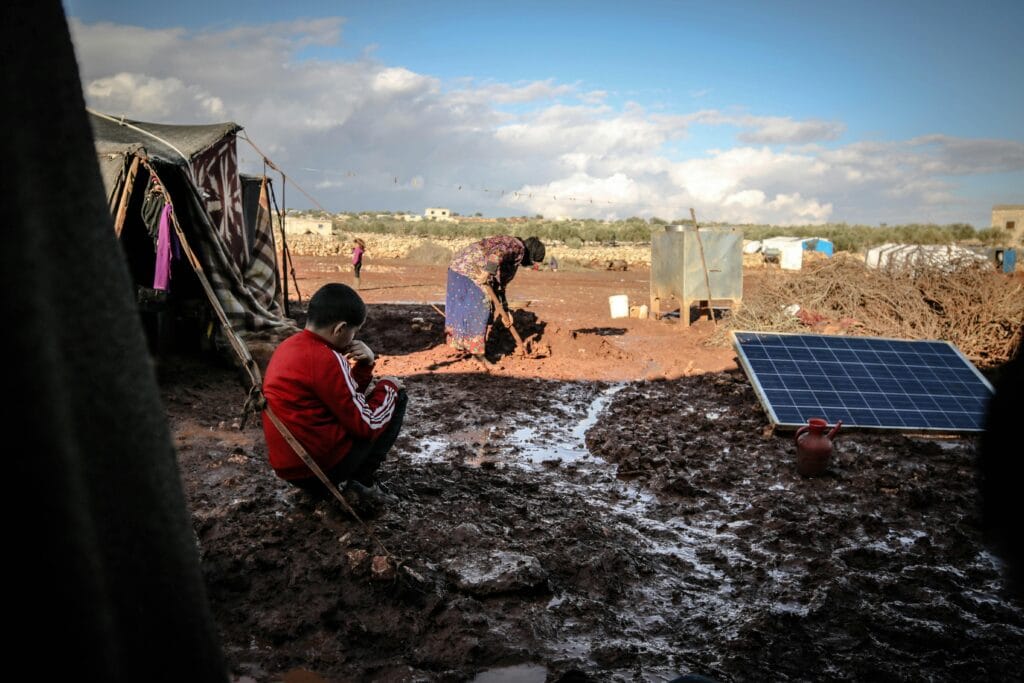 pexels-photo-10629462-10629462 A boy and woman in a muddy refugee camp in Idlib, Syria with tents and solar panel.