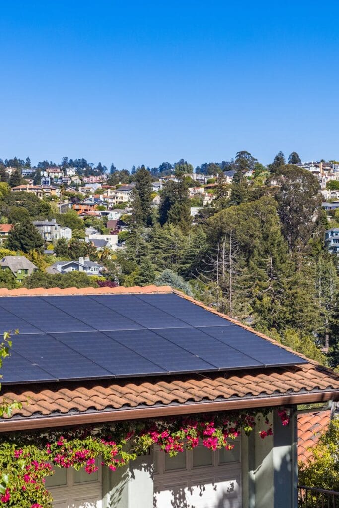 Solar panels on a suburban home, surrounded by lush greenery and a sunny blue sky.